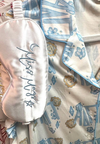 Sleep mask with 'Miss Mags' embroidery on a patterned fabric background